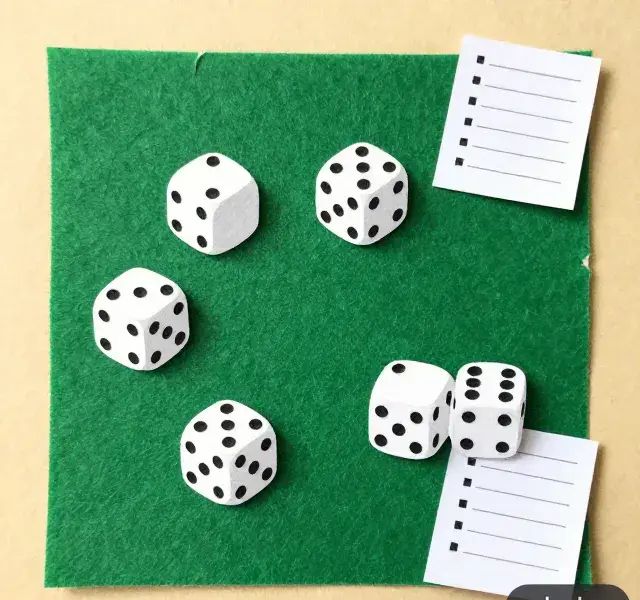 Six paper-cutout dice on green felt with a cut-paper score sheet